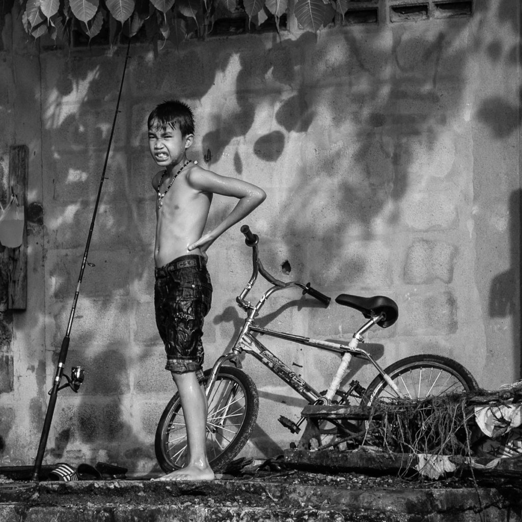 a wet shirtless boy with bike and fishing pole.