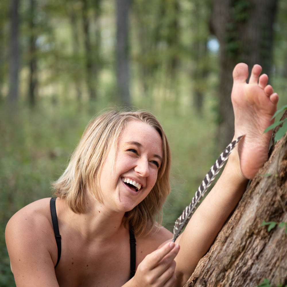 girl tickling soles of her bare feet with a turkey feather