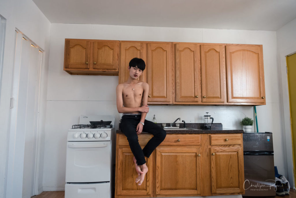 barefoot and shirtless asian teenager sitting on kitchen counter