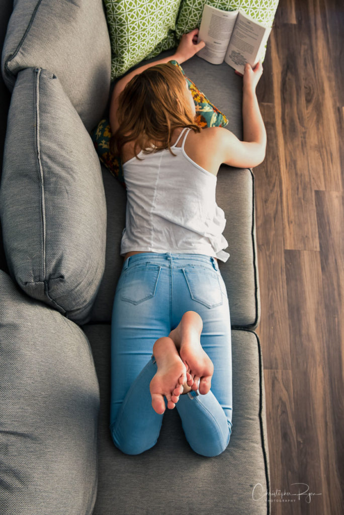 female teenager reading a book on the sofa with her bare soles pointed upwards