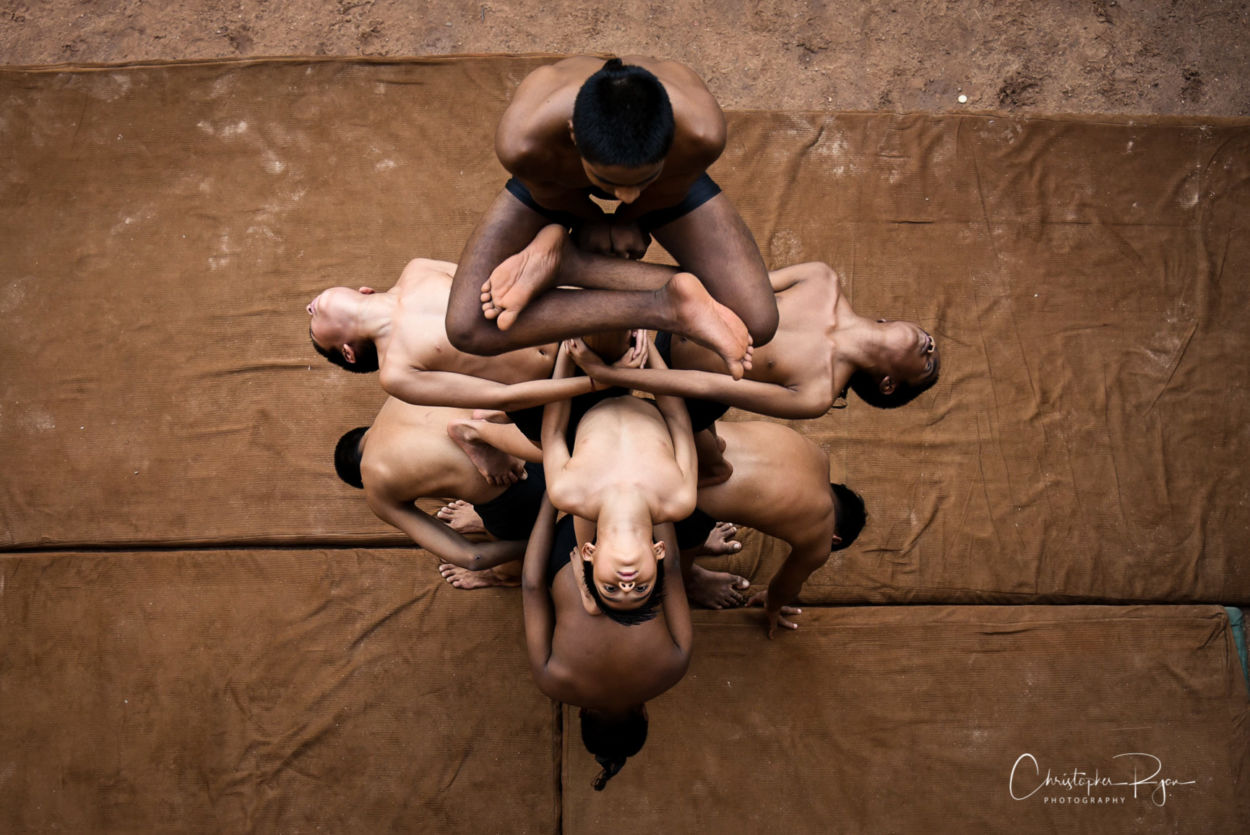 overhead view of mallakhamb performers shows nicely defined shirtless young boys close together