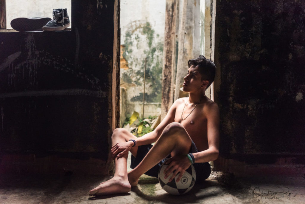 shirtless and barefoot teen with soccer ball.