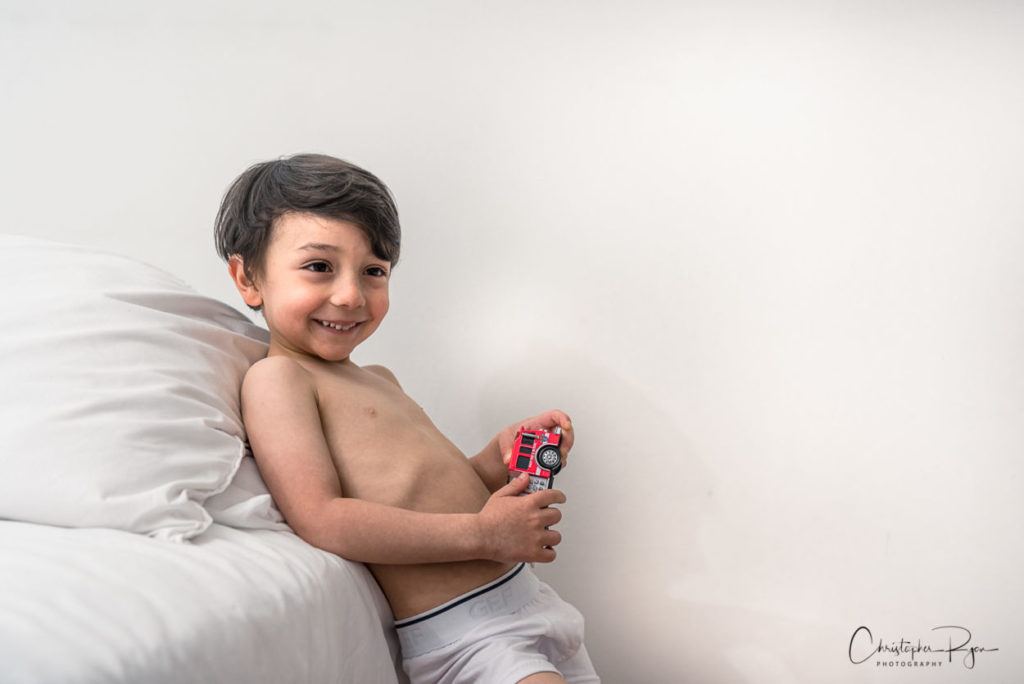 shirtless five year old boy in white underwear playing with red toy truck