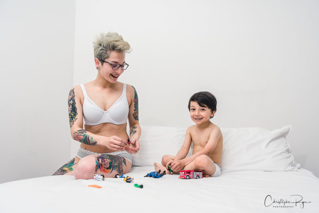 Tattooed mom and son playing with toys on a bed