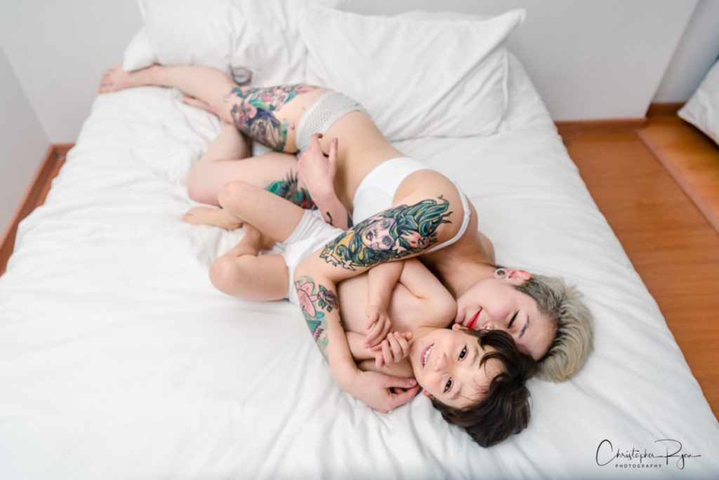 young boys and mother with colorful tattoos laying in bed snuggling