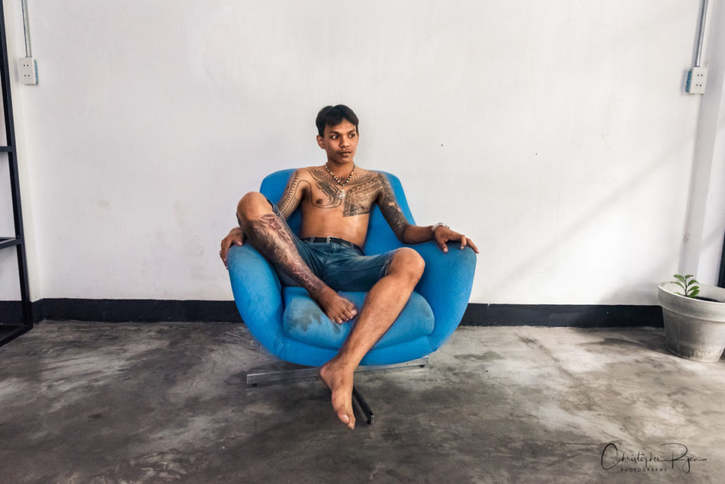 shirtless barefoot teen boy in blue chair with beautiful tattoos