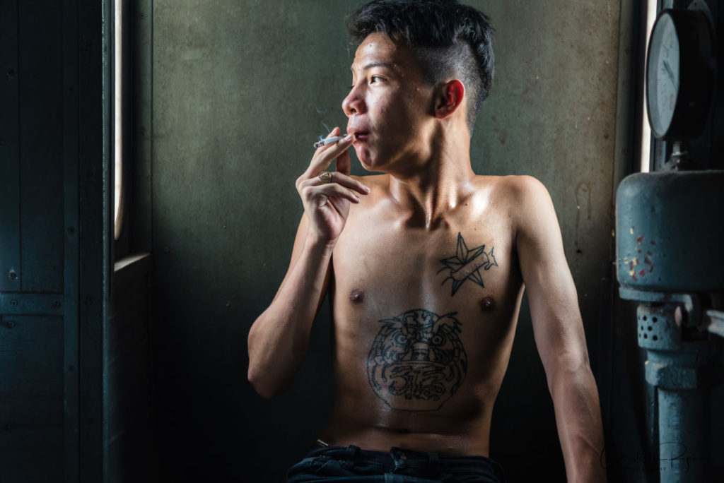 shirtless teenager with tattoos smoking a cigarette