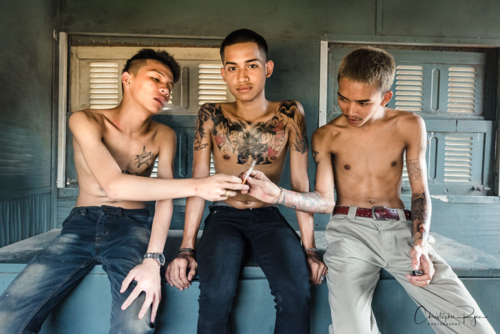 three shirtless boys sharing a cigarette