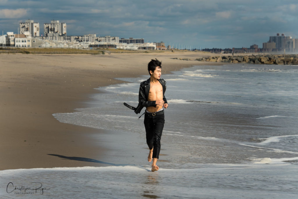 barefoot teen boy in open leather jacket and no shirt running on the beach in New York