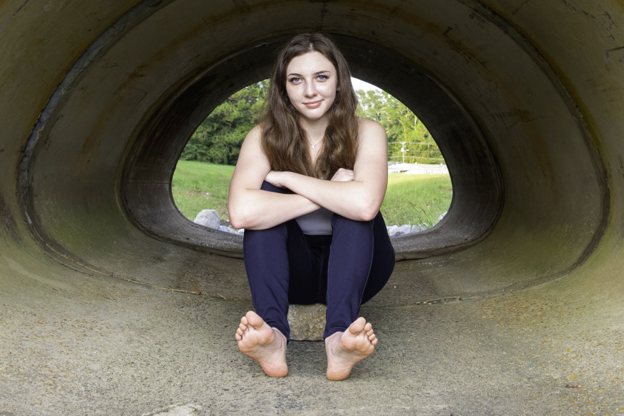 Barefoot girl sitting in a culvert pipe